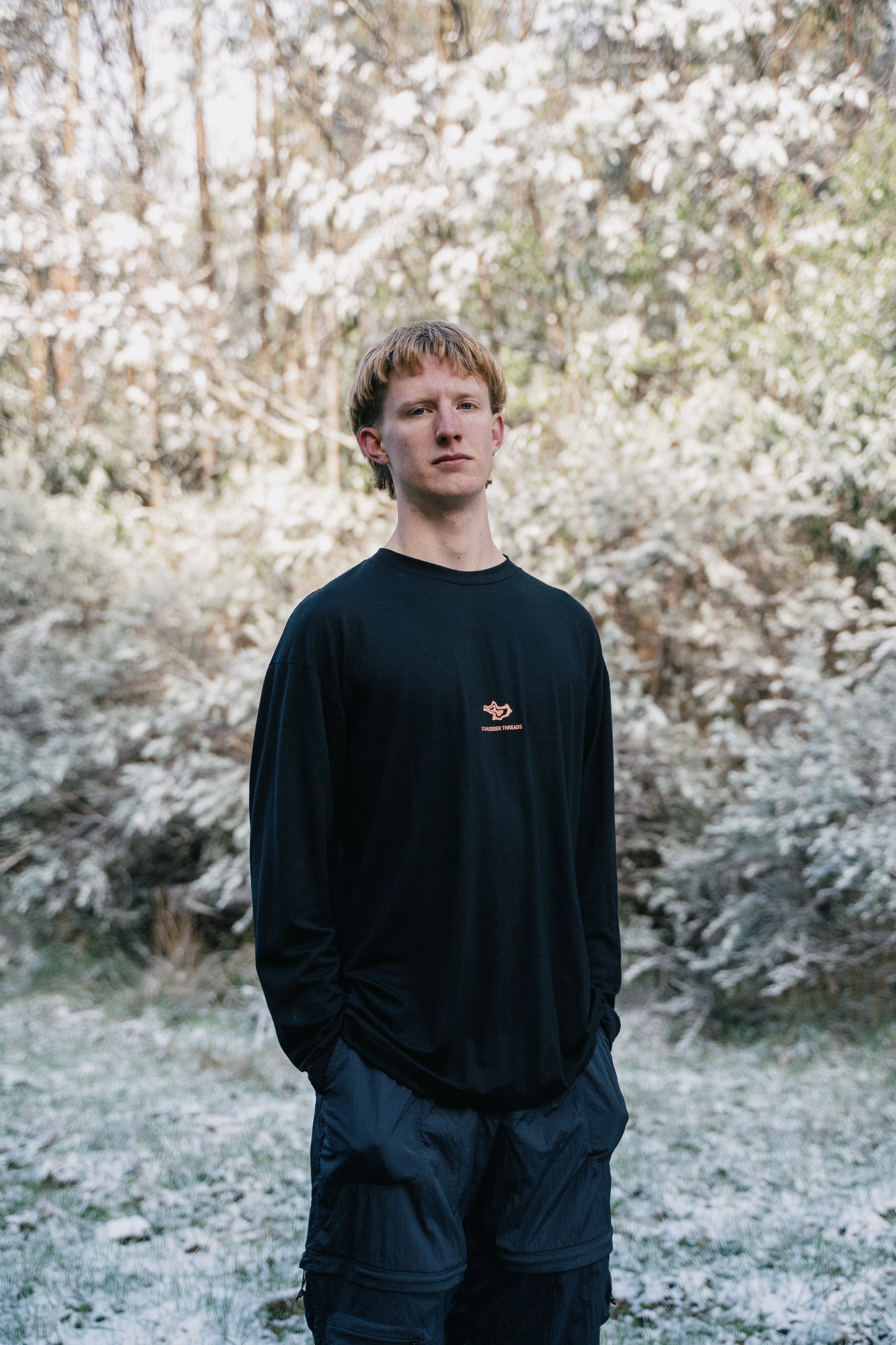 A man standing in a landscape lightly dusted with snow wearing a black shirt and black pants.