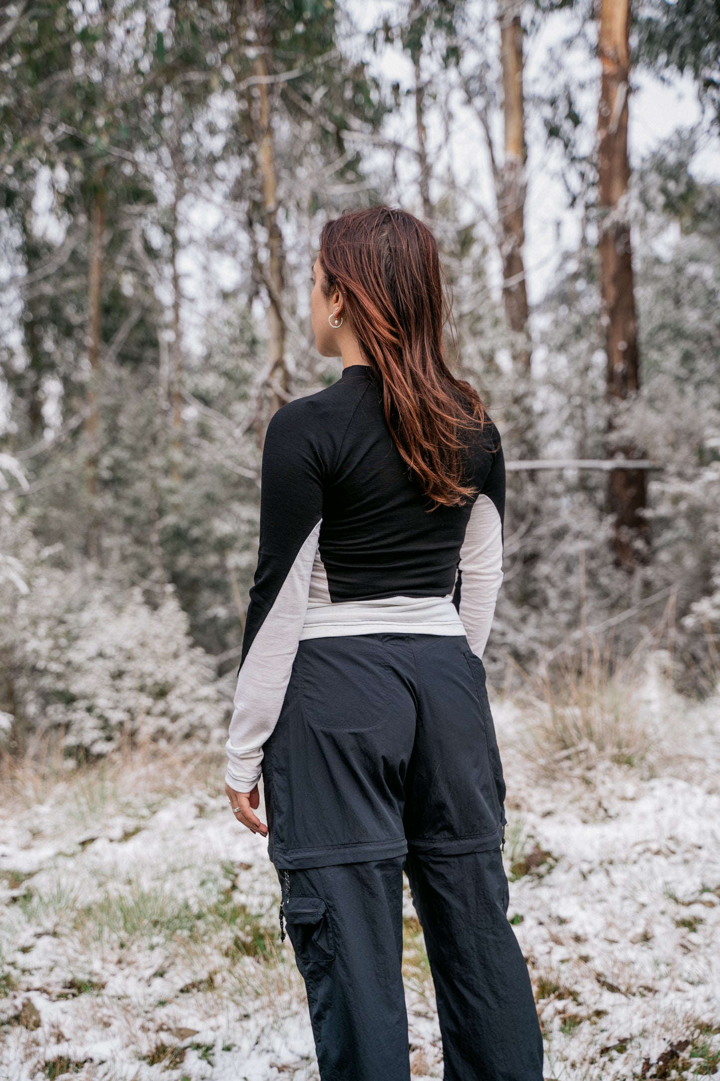 A woman wearing a half white-half black merino shirt in the snow facing away from the camera.