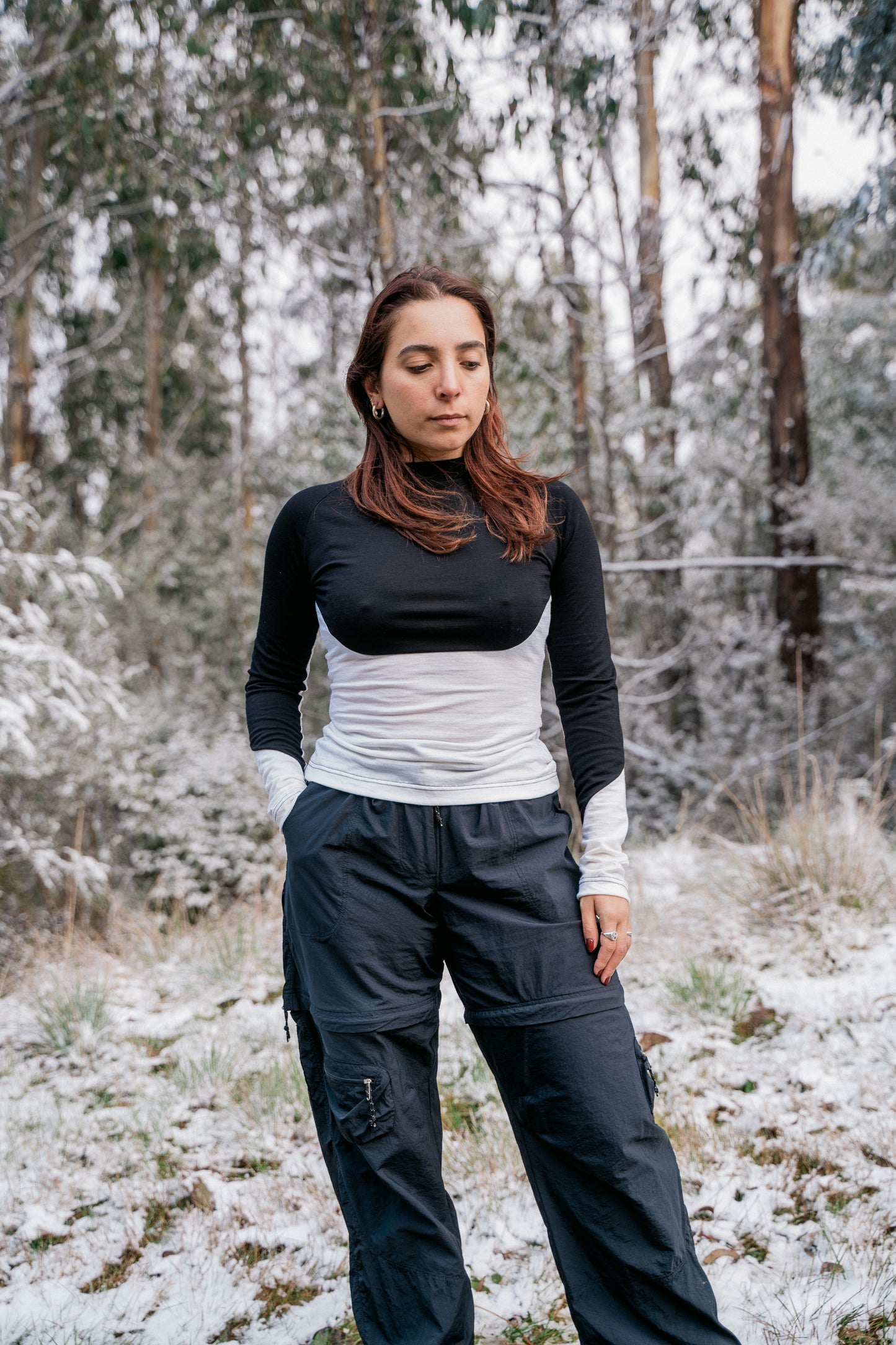 A woman wearing a half white-half black merino shirt in the snow facing towards the camera.