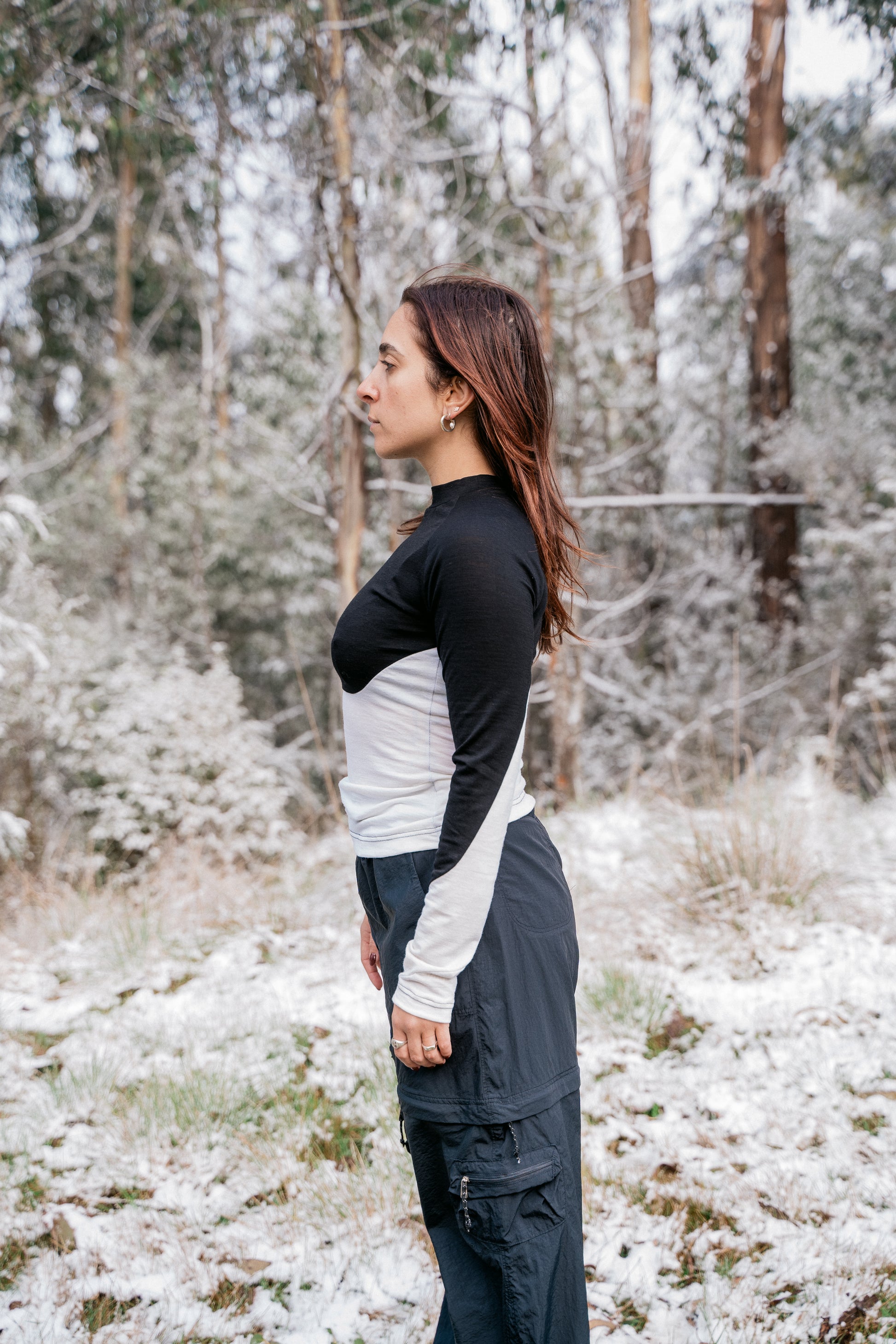 A woman wearing a half white-half black merino shirt in the snow facing to the side.