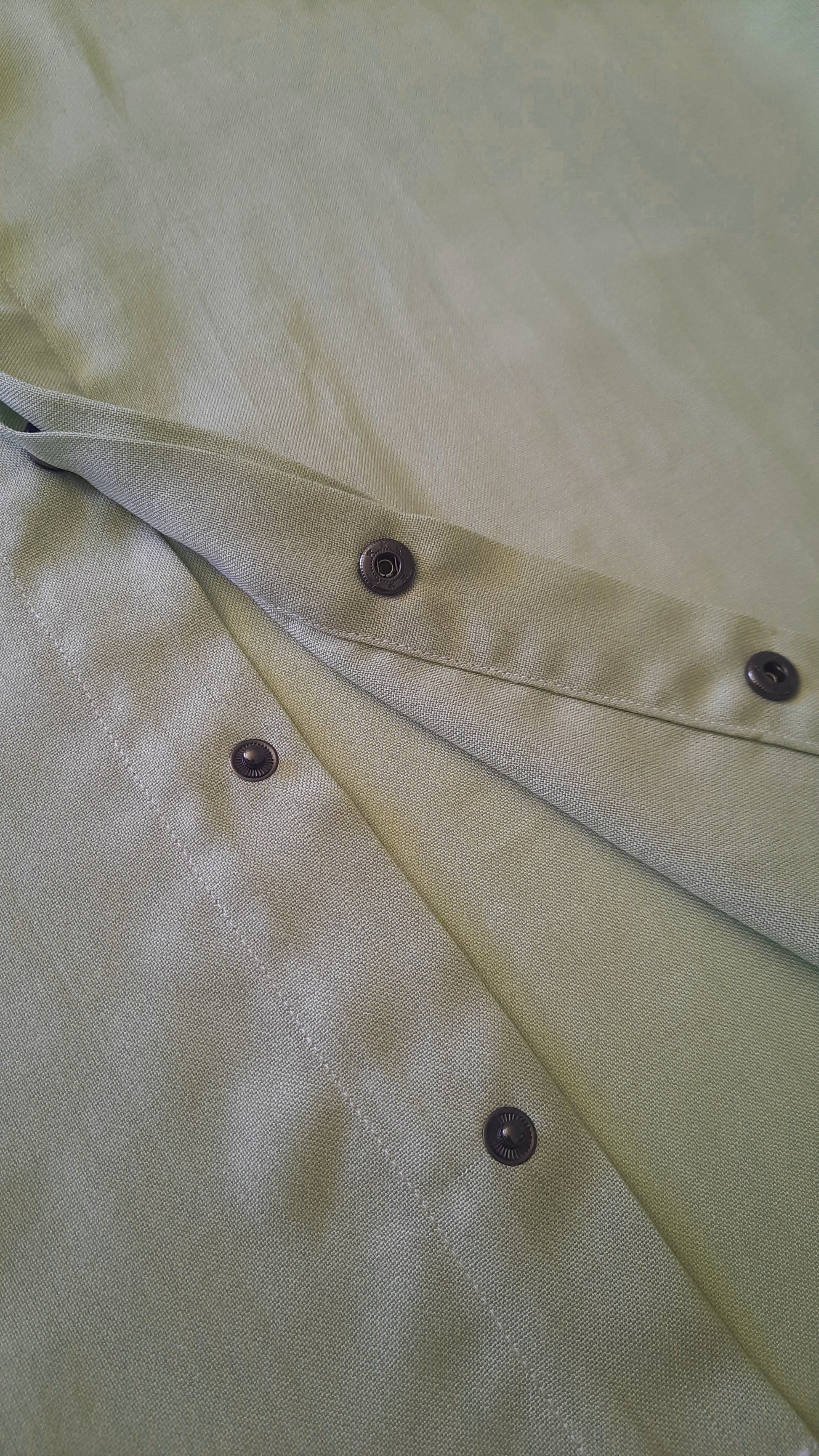 A close up image of a green shirt placket with snap opening.