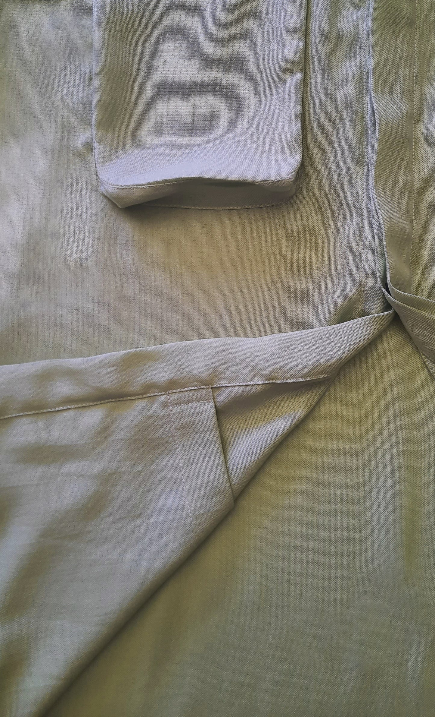 a closeup image of a green shirt with the front folded up to see the internal pocket. 