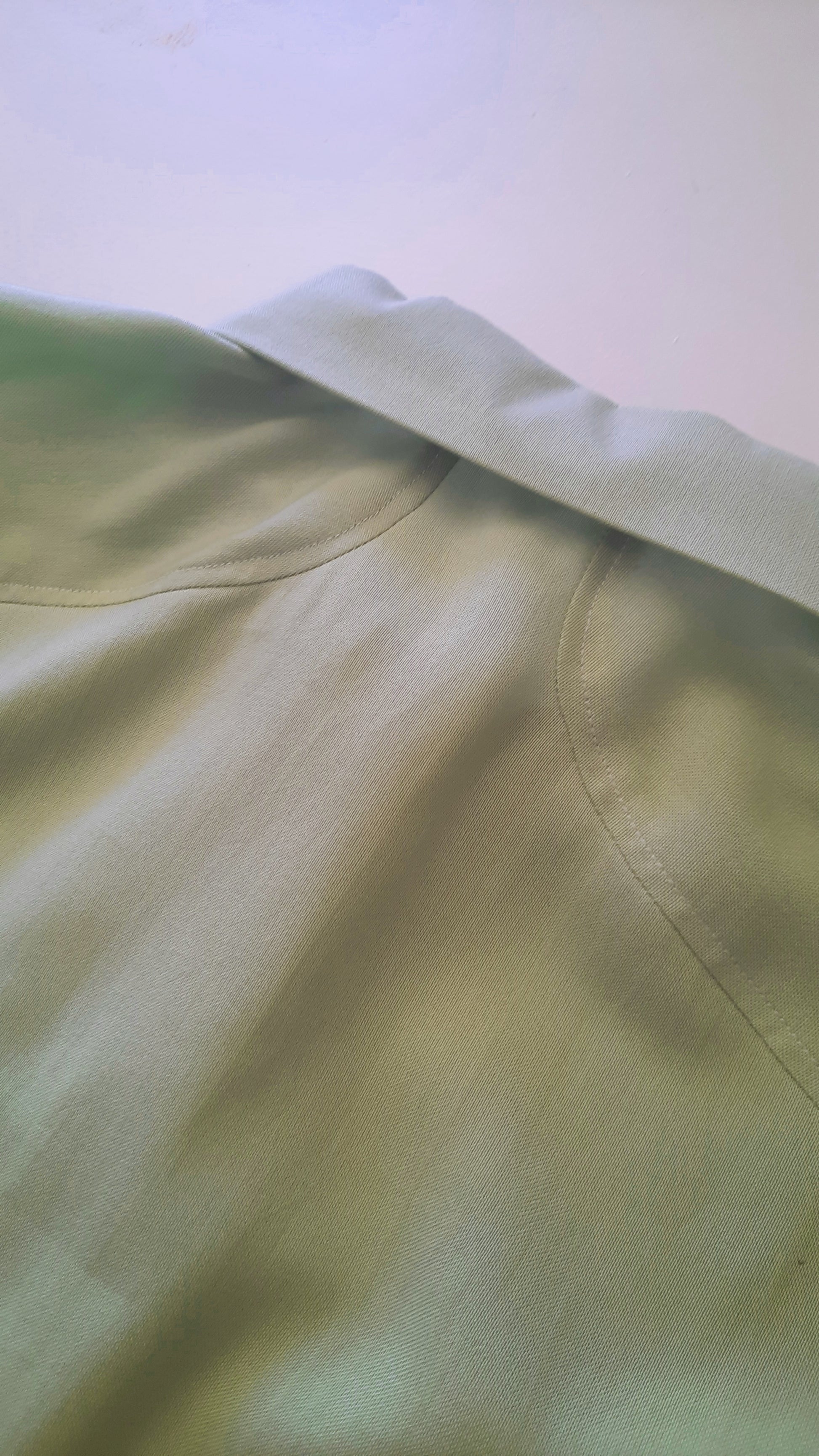 A closeup image of a green shirt back with a collar and the back seam detailing.