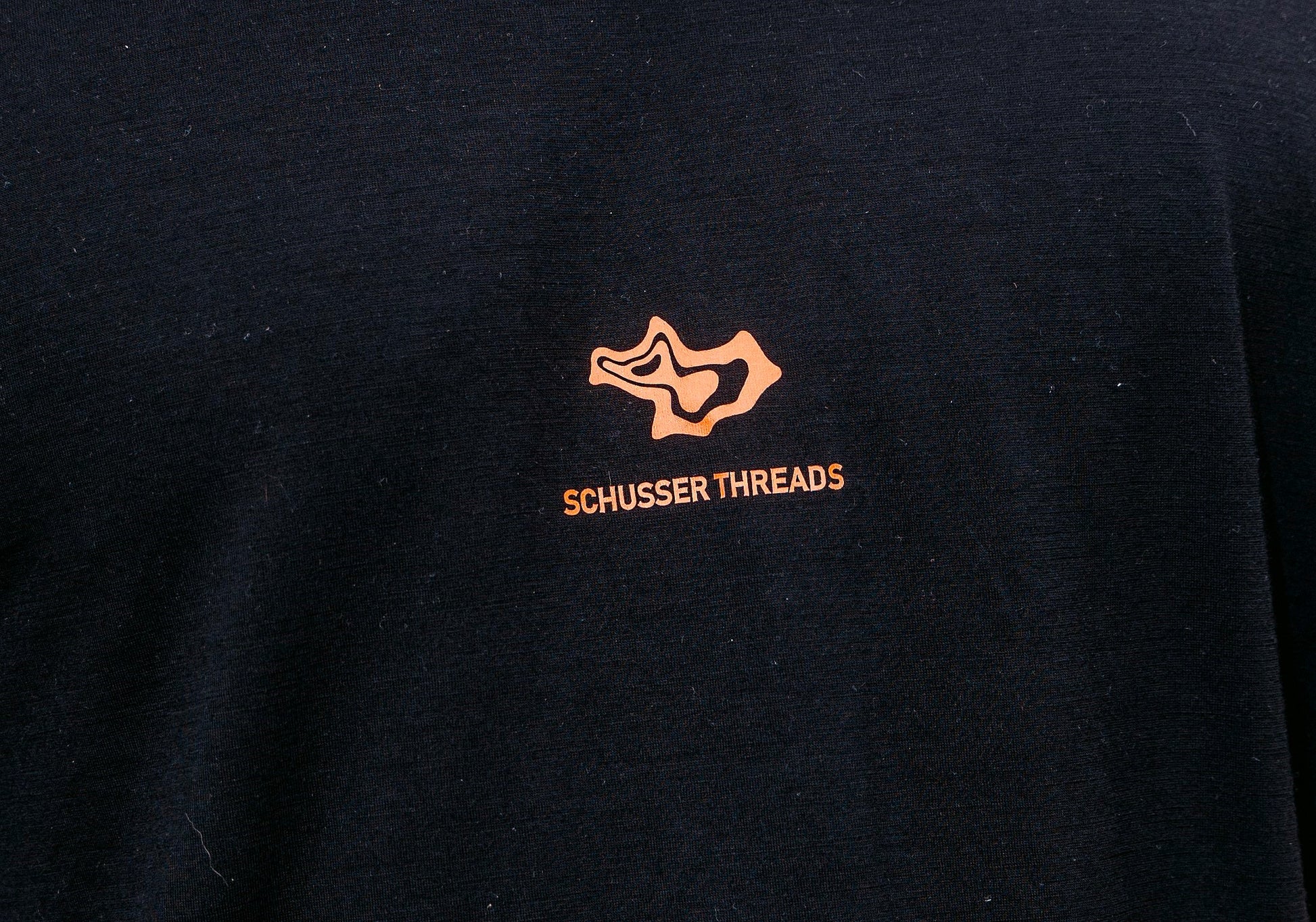 a detail shot of the peach coloured schusser threads logo on a black merino base.